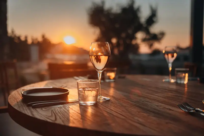Une table en bois est dressée avec de la vaisselle et des verres devant un coucher de soleil.