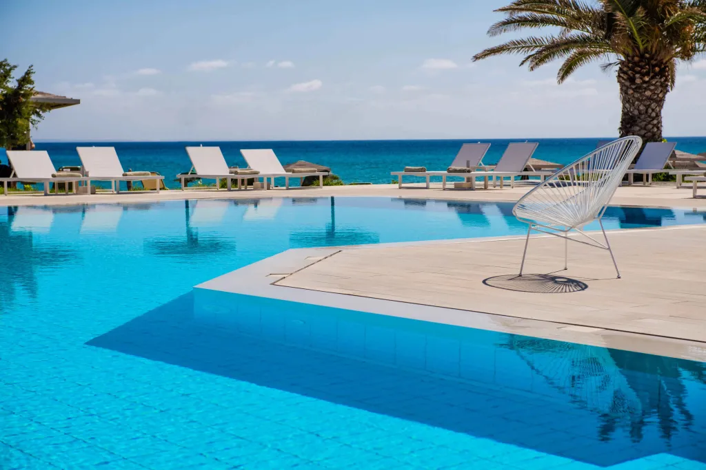 Une piscine bleue bordée de transats blancs avec vue sur la mer.