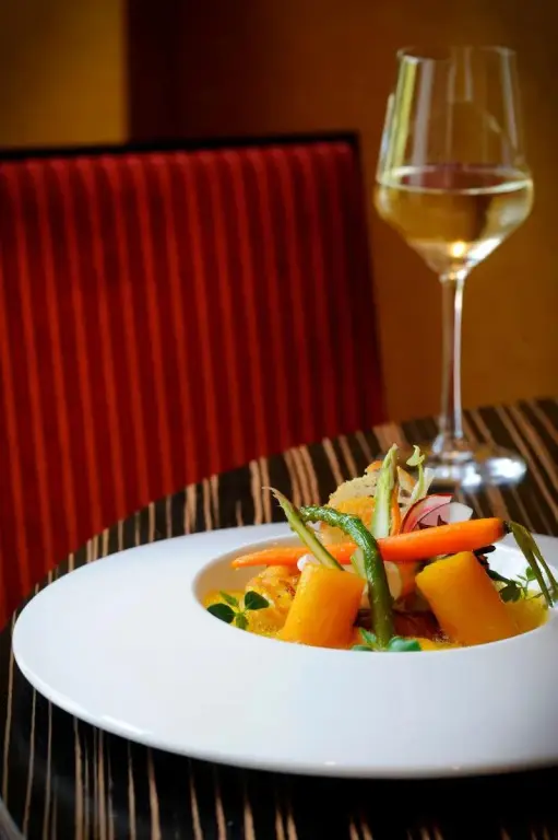 Assiette de légumes colorés et verre de vin sur une table.