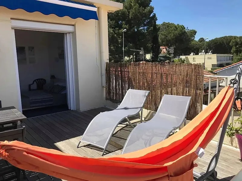 Terrasse ensoleillée avec transats et hamac rouge.