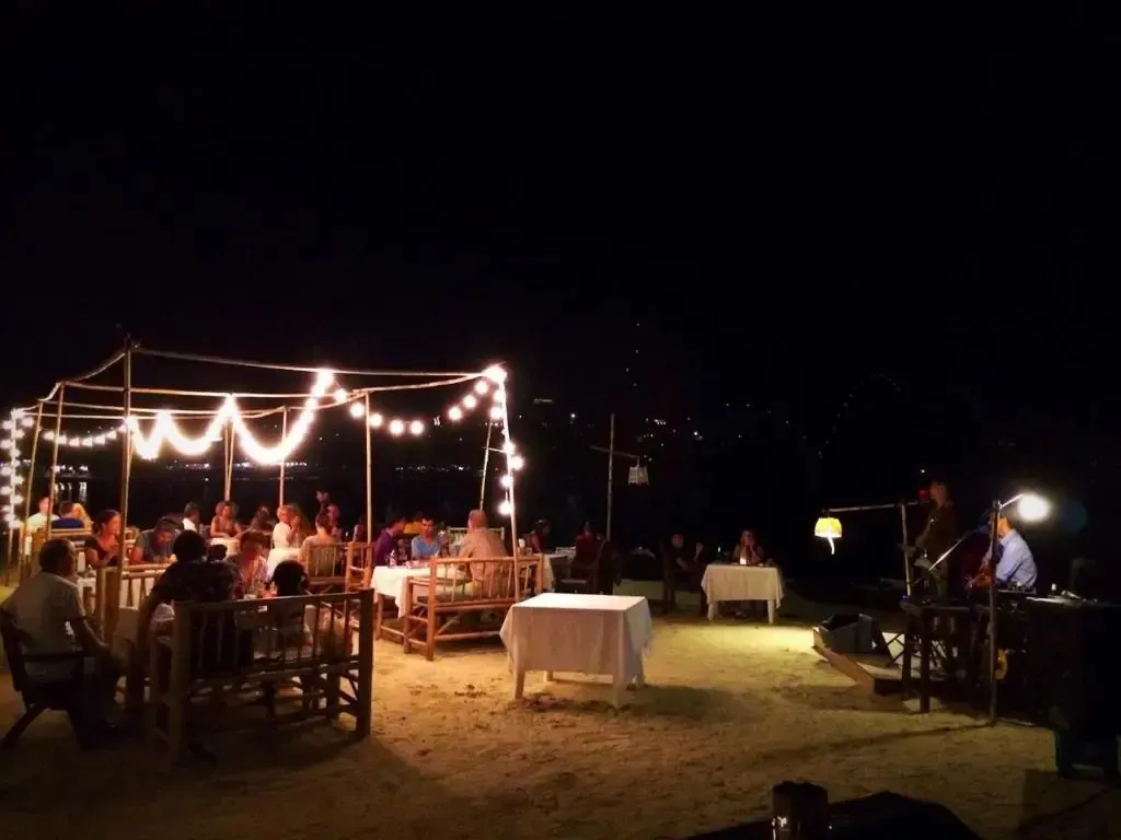 Une terrasse éclairée accueille des convives autour de tables en soirée.