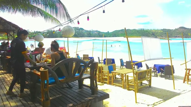 Tables et chaises en bois sur une terrasse de plage ensoleillée.