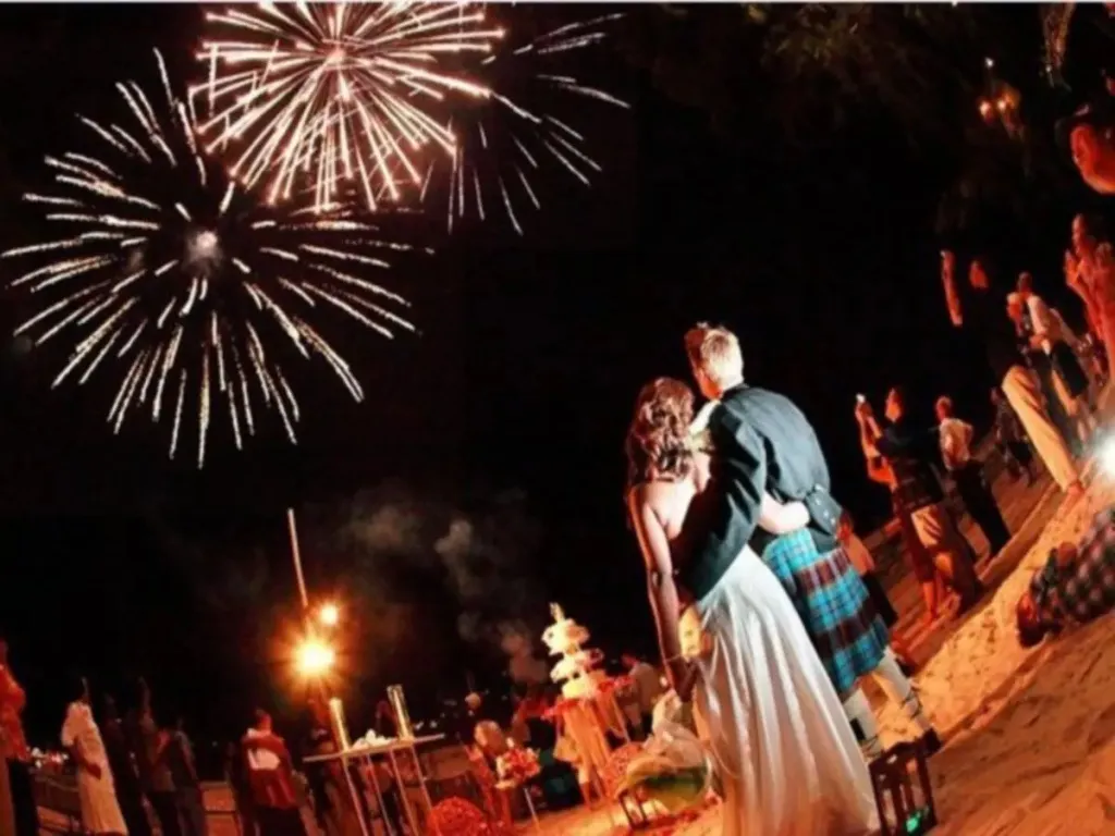 Un couple s'embrasse sur une plage illuminée par des feux d'artifice.