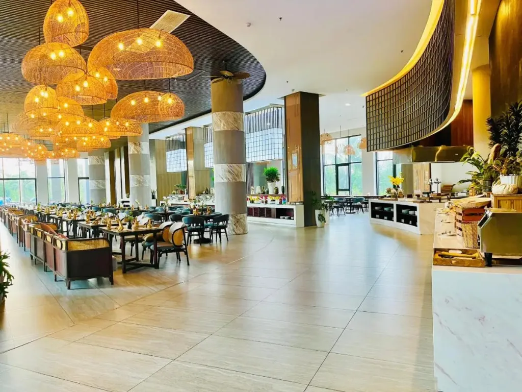 Une grande salle lumineuse est aménagée en espace de restauration avec des tables dressées et un buffet.