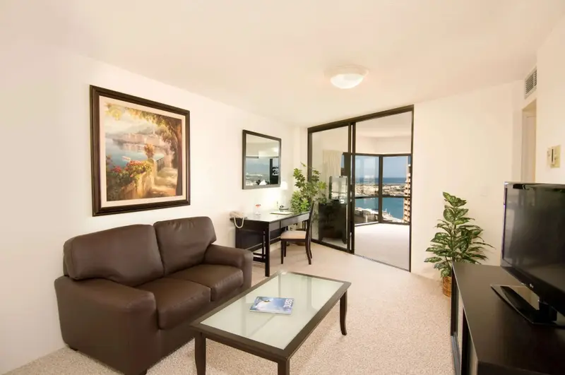 Un salon clair avec un canapé marron et un bureau près d'une baie vitrée.