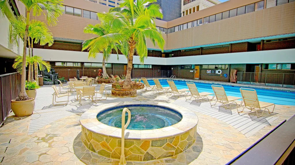 Une piscine ensoleillée avec des transats et un jacuzzi au premier plan.