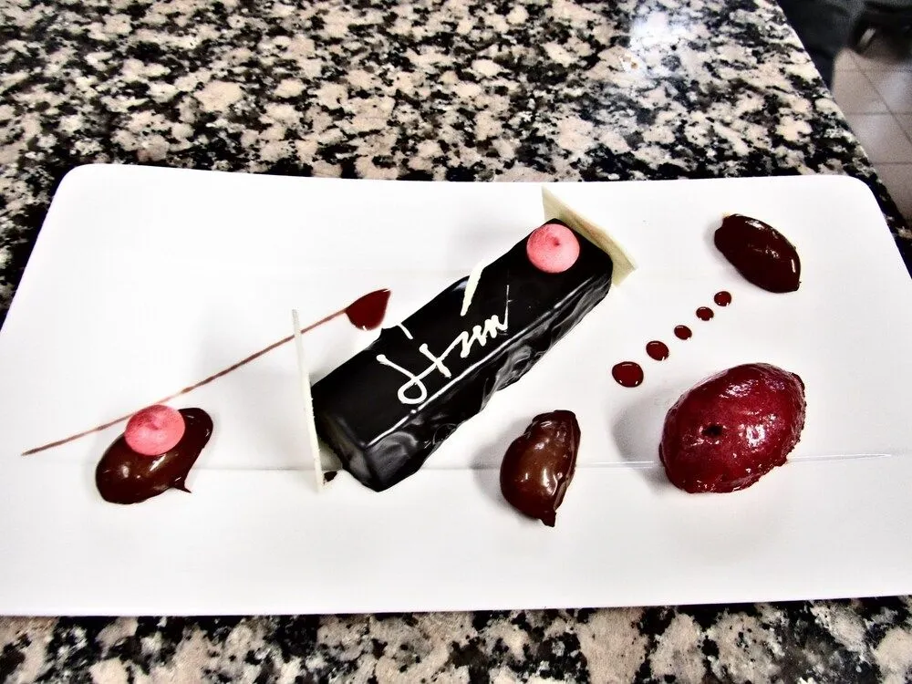 Présentation d'un dessert au chocolat décoré de fruits rouges sur une assiette blanche.