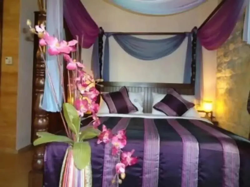 Un lit à baldaquin est décoré de tissus violets et blancs.