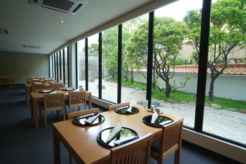 Une salle lumineuse avec des tables dressées face à un jardin verdoyant.