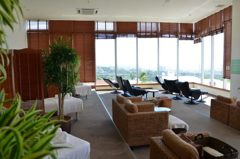Espace de détente lumineux avec mobilier en rotin et vue sur un paysage verdoyant.