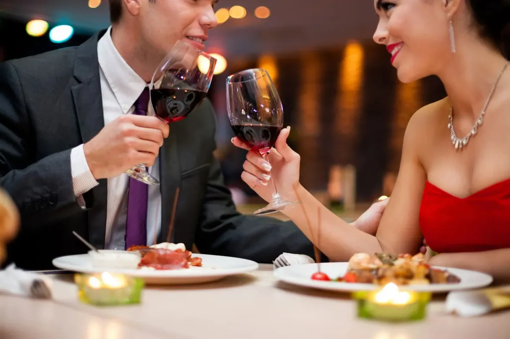 Un couple trinque avec des verres de vin rouge lors d'un dîner.