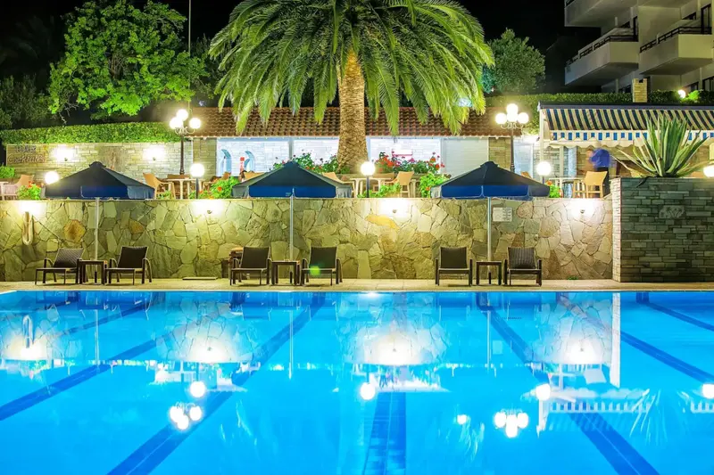 Piscine illuminée avec transats et parasols, devant un restaurant en terrasse.