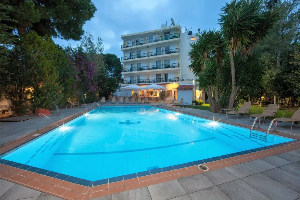 Une piscine rectangulaire illuminée au crépuscule, avec un bâtiment à plusieurs étages en arrière-plan.