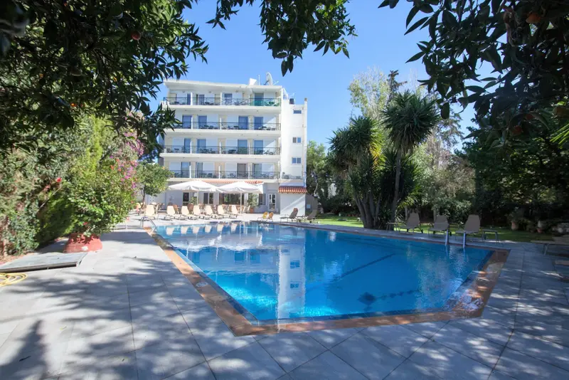 Une piscine rectangulaire bordée d'un dallage clair, avec un bâtiment blanc en arrière-plan.