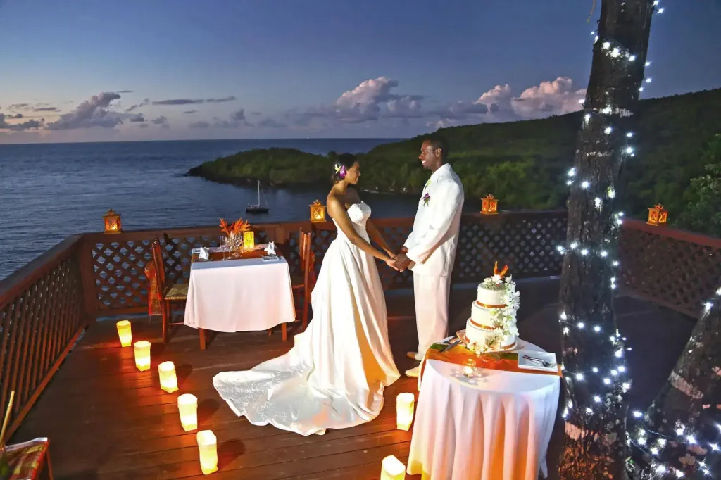 Un couple en tenue de mariage se tient sur une terrasse illuminée face à la mer.