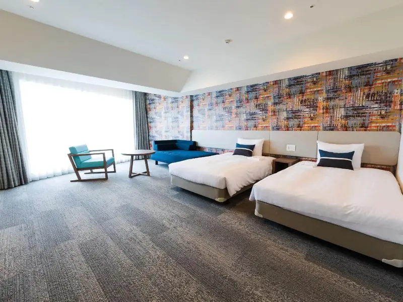 Une chambre lumineuse avec deux lits simples et un coin salon près d'une fenêtre.