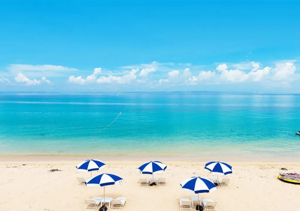 Plage de sable fin bordée de parasols bleus et de chaises longues.
