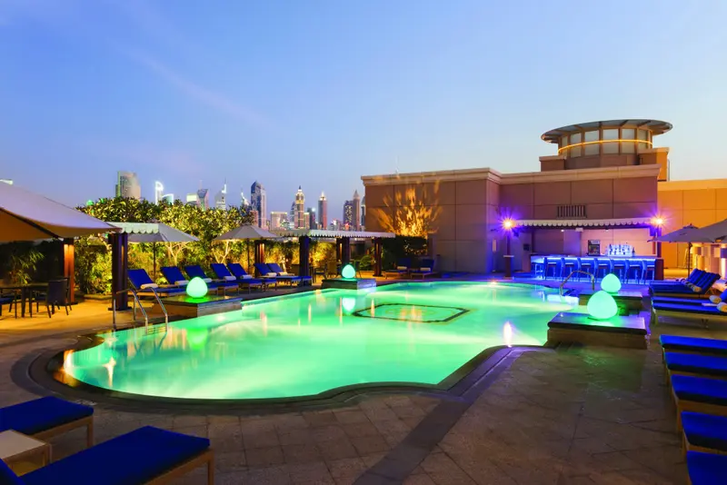 Une piscine illuminée avec des transats et un bar en soirée.