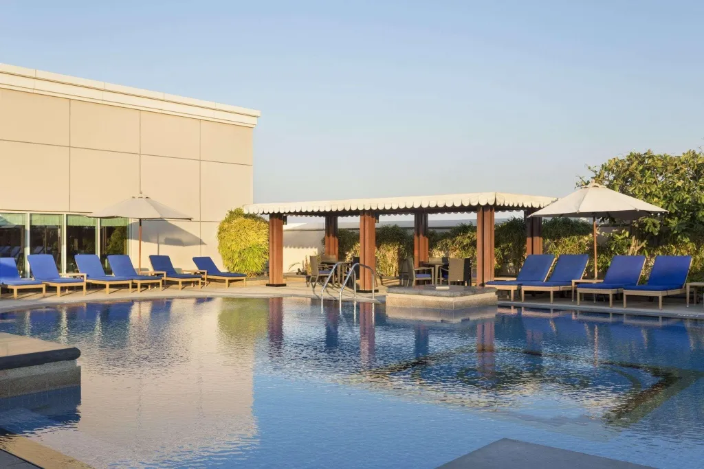 Une piscine bleue avec des transats bleus et un espace ombragé avec des tables.