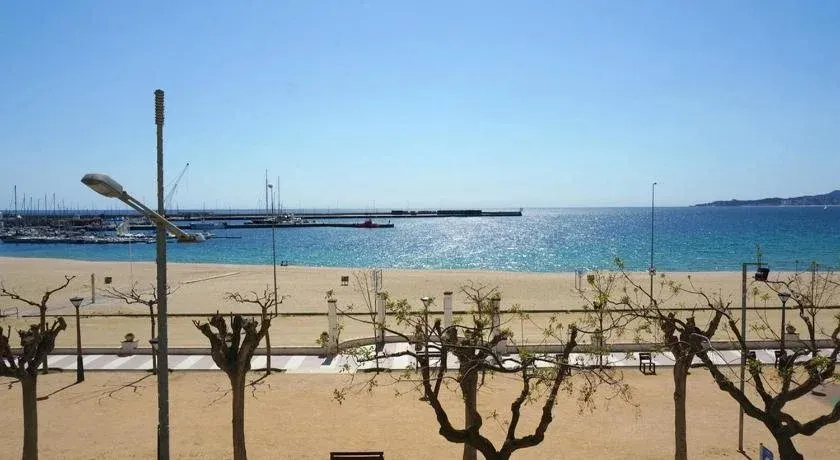 Vue ensoleillée sur une plage de sable fin bordée d'une promenade et d'un port de plaisance.