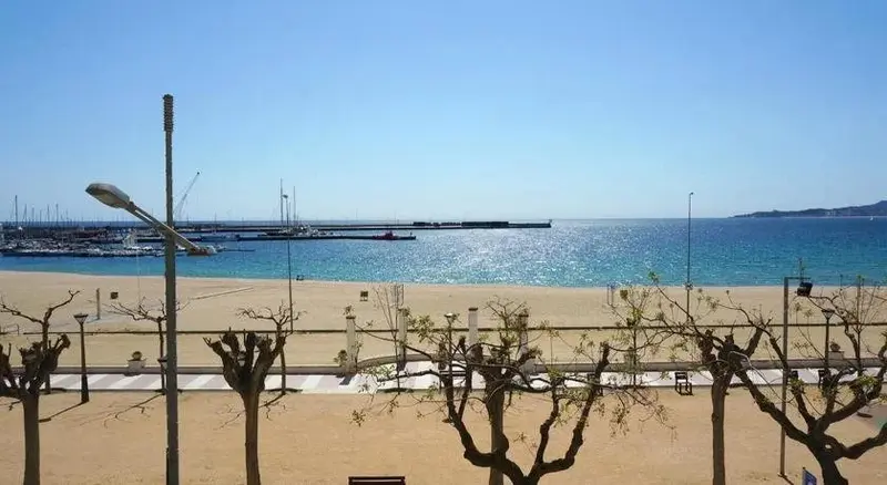 Vue ensoleillée sur une plage de sable fin bordée d'une promenade et d'un port de plaisance.