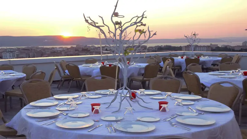 Tables dressées en extérieur avec vue sur une ville au coucher du soleil.