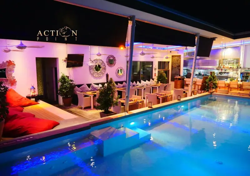 Une piscine illuminée avec des tables et des chaises disposées sur le bord.