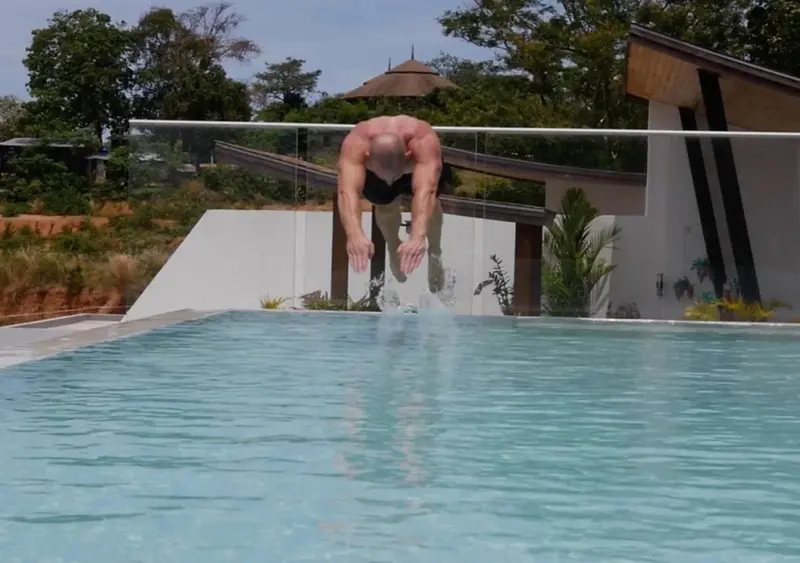 Un homme saute dans une piscine rectangulaire bordée d'une terrasse.