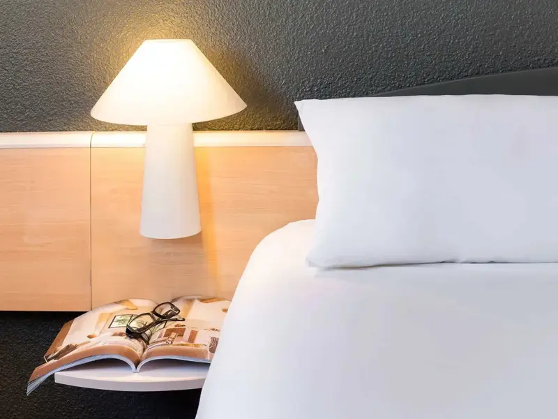 Un lit blanc avec une lampe de chevet sur une table en bois.