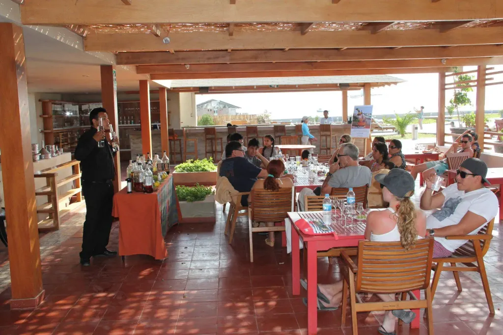 Des clients sont servis à une terrasse ombragée avec un bar en fond.