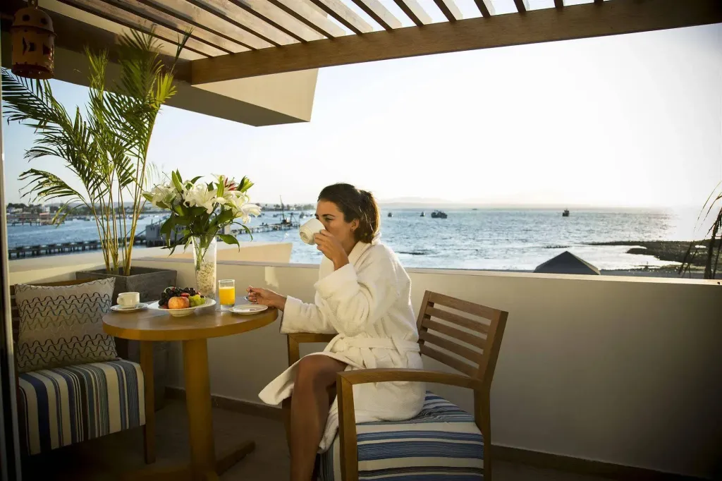 Une femme prend son petit-déjeuner sur une terrasse ensoleillée avec vue sur la mer.