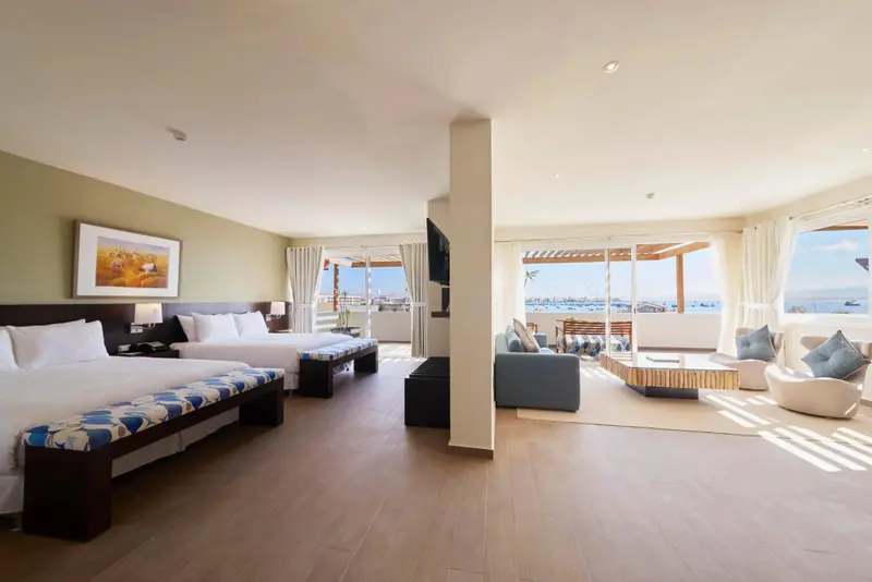 Espace de vie lumineux avec lits et coin salon offrant une vue sur la mer.