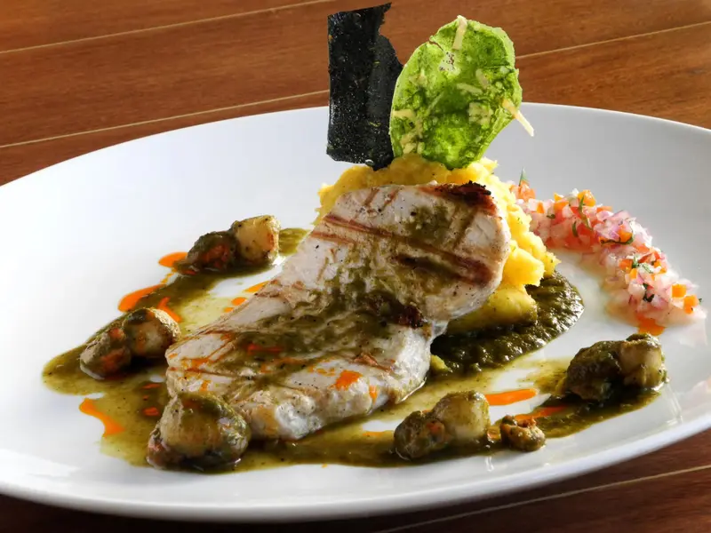 Assiette de poisson grillé accompagnée de légumes et de sauces colorées.
