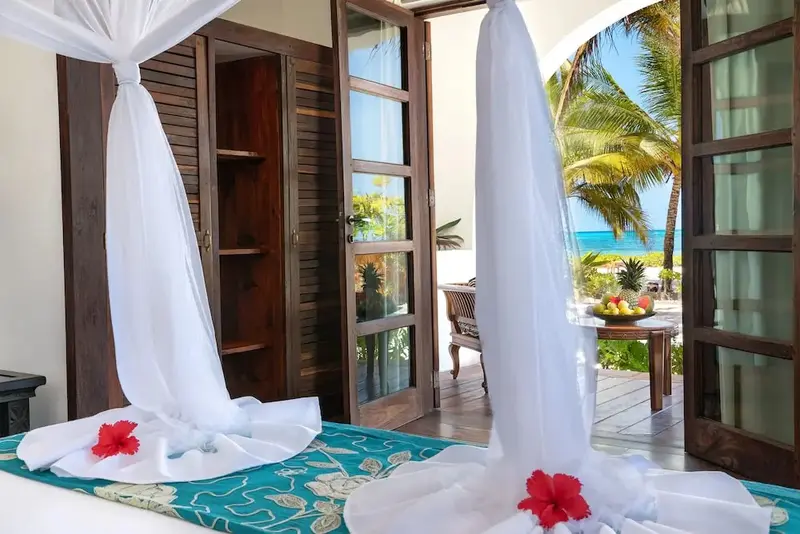 Un lit à baldaquin décoré de fleurs rouges s'ouvre sur une terrasse ensoleillée avec vue sur la mer.
