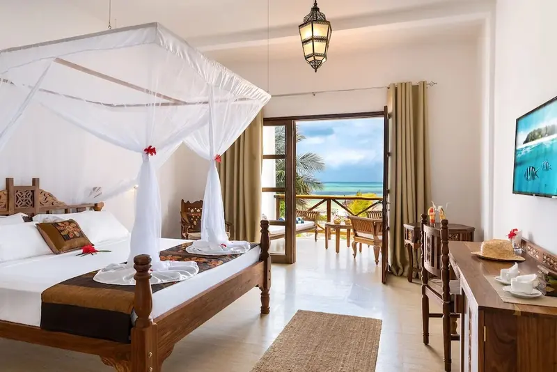Chambre lumineuse avec un grand lit à baldaquin donnant sur une vue mer.