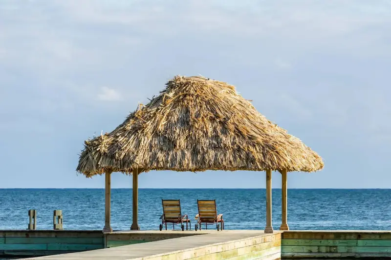 Deux fauteuils de jardin sont placés sous un abri de chaume sur une jetée.
