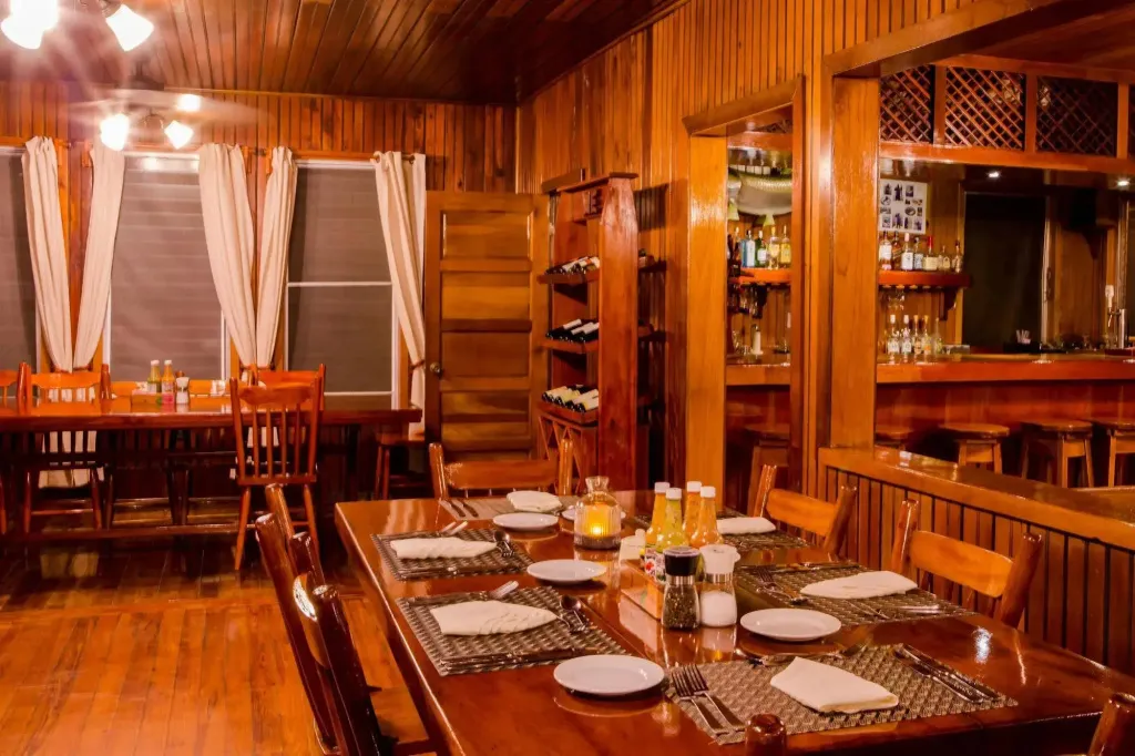 Une salle à manger en bois avec des tables dressées et un bar en fond.
