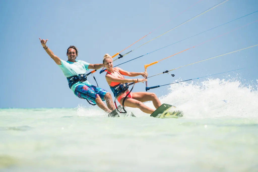 Deux personnes pratiquent le kitesurf sur une eau turquoise sous un ciel bleu.