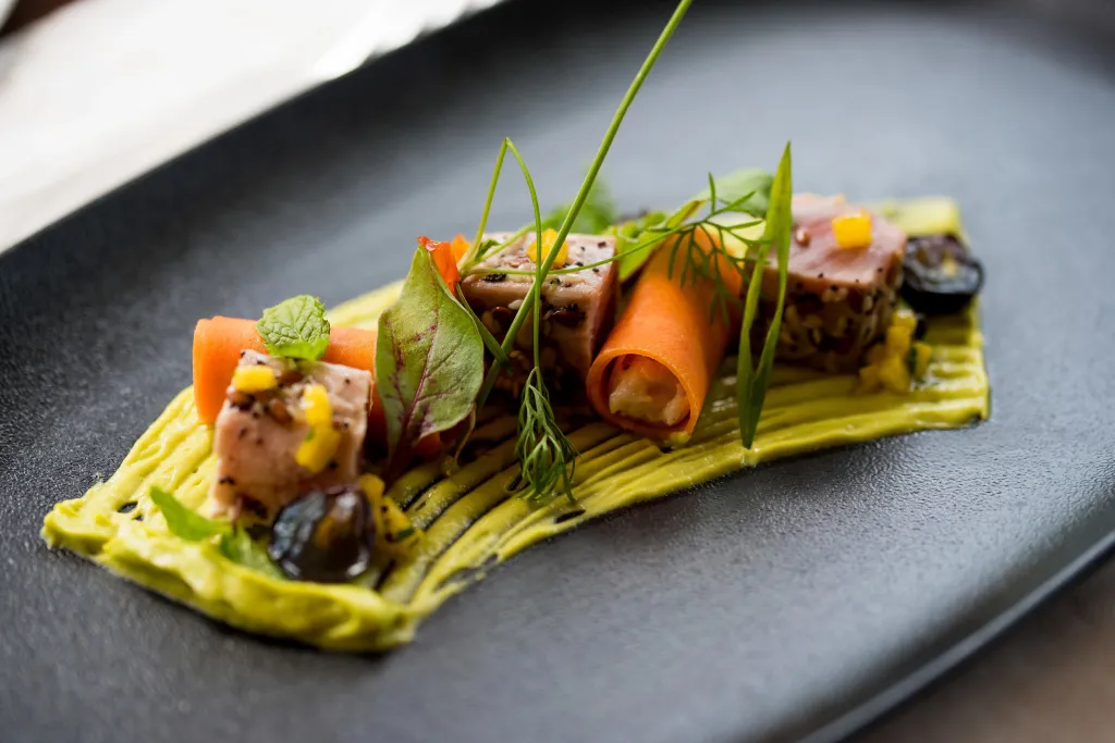 Assiette raffinée avec des morceaux de poisson, des légumes et une sauce verte.