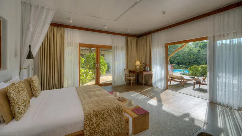 Une chambre lumineuse s'ouvre sur une terrasse avec vue sur la végétation et une piscine.