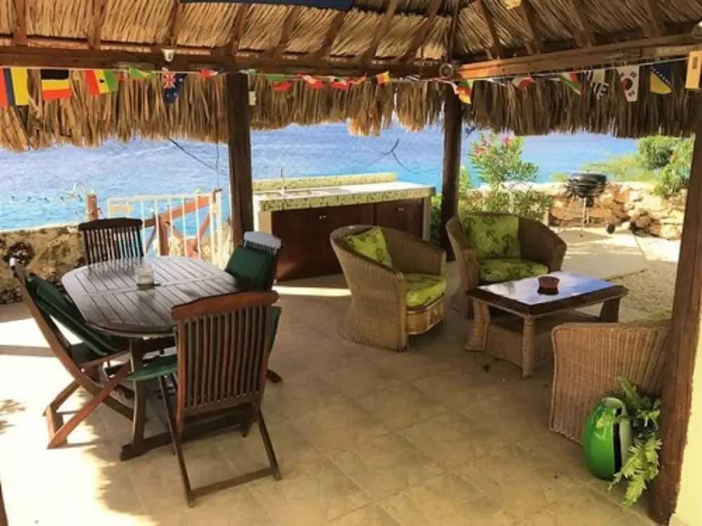 Espace repas extérieur ombragé avec mobilier en rotin et vue sur la mer.