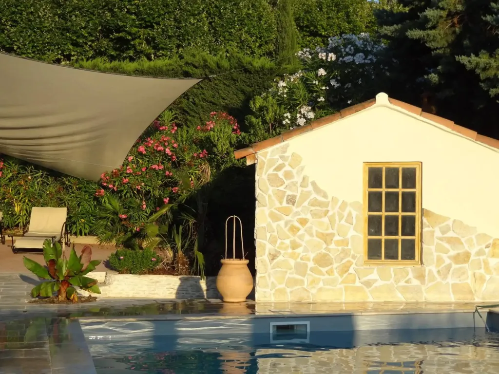 Un bâtiment en pierre claire se trouve au bord d'une piscine ensoleillée.