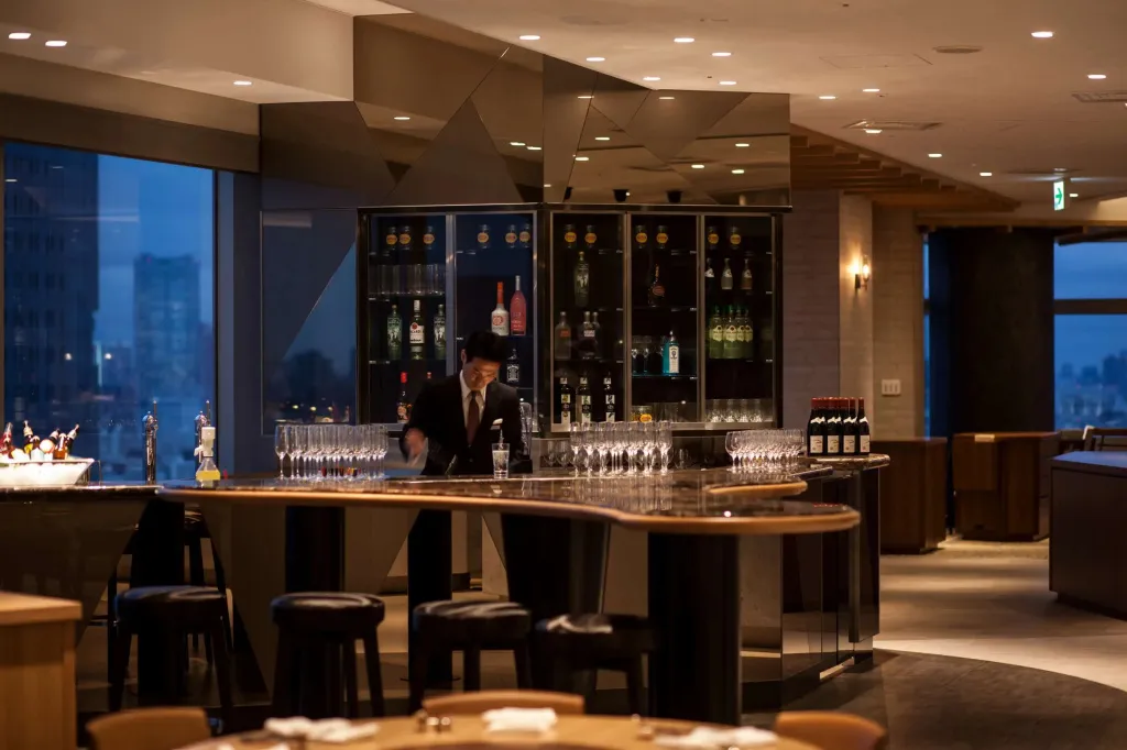 Un barman prépare des boissons derrière un comptoir illuminé dans un espace élégant.