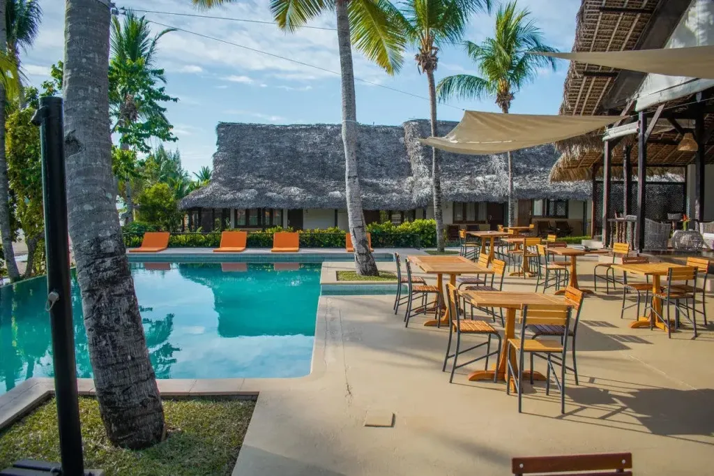 Une piscine turquoise bordée de chaises longues et d'une terrasse ombragée avec des tables et des chaises.