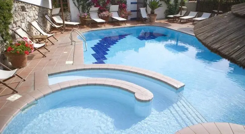 Une piscine bleue avec des transats et des plantes environnantes.