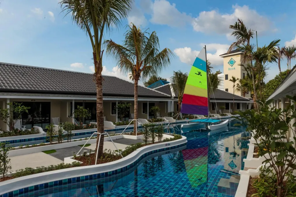 Une piscine sinueuse relie plusieurs bâtiments bas aux toits sombres.