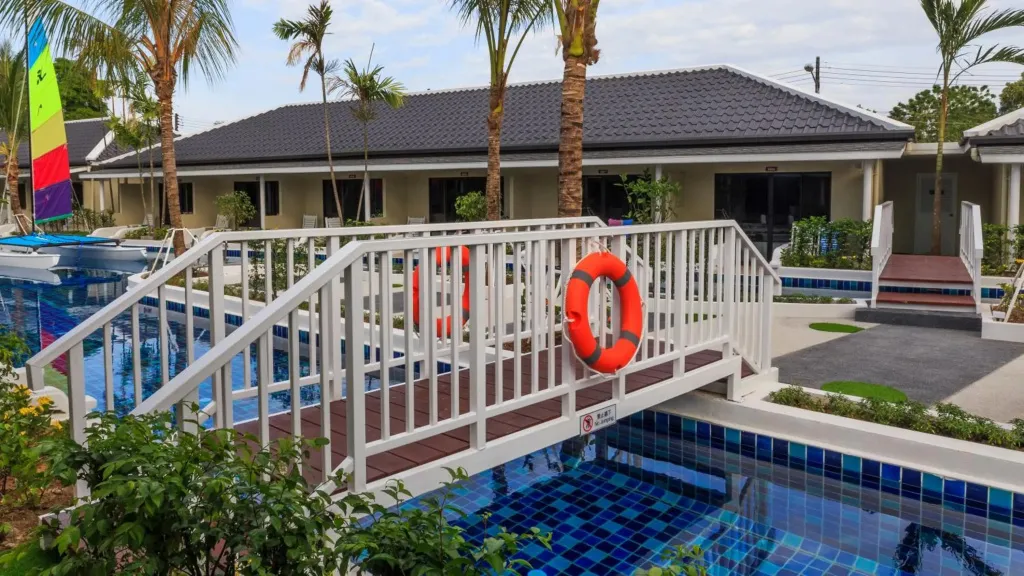 Un ponton en bois blanc enjambe une piscine turquoise bordée de végétation.