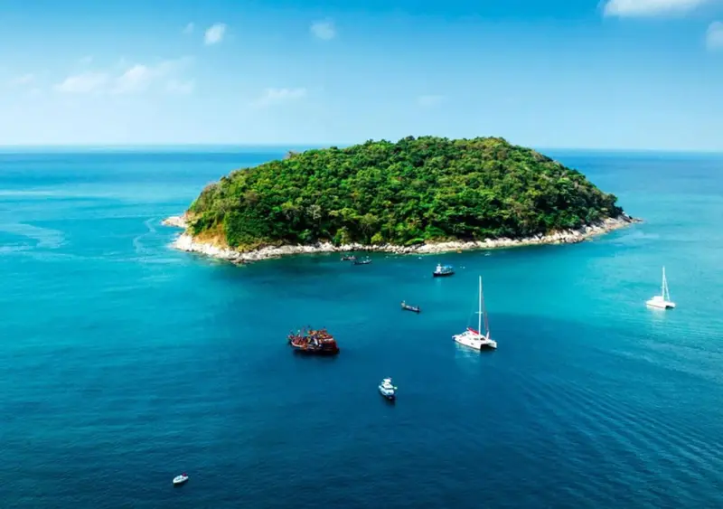 Une île verdoyante entourée d'une mer bleue et de plusieurs bateaux.