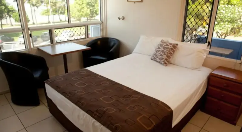 Une chambre lumineuse avec un lit double, une table et deux chaises près d'une fenêtre.