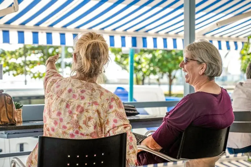 Deux femmes discutent autour d'une table en extérieur sous un auvent rayé.